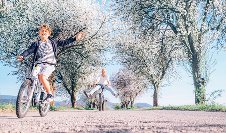 Father and son having fun spreading wide legs when riding bicycles on country road under blossom trees. Healthy sporty lifestyle concept image.の写真素材