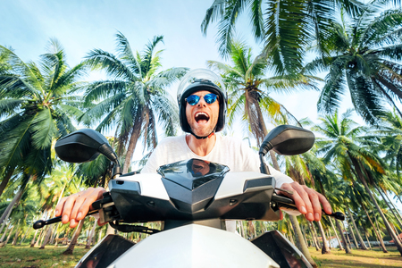 Man in safe helmet riding a motorbike under palm trees wide angle lens shotの写真素材