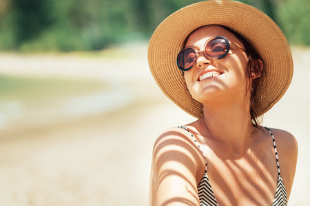 Happy smiling sun buthing woman in straw hat portrait. Palm tree shadows on the body. Health tanning concept の写真素材