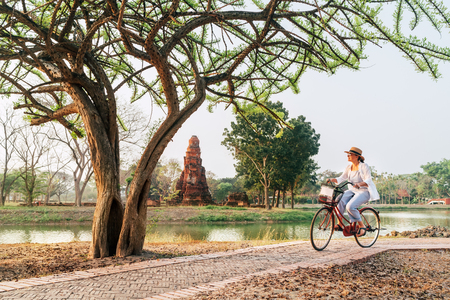 Female traveler weared light summer clothes and hat have early morning bicycle walk in Ayutthaya historical park, Thailandの写真素材