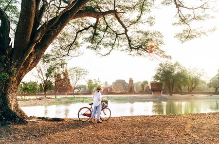 Female traveler weared light summer clothes and hat have early morning walk with bicycle near pond in Ayutthaya historical park,Thailandの写真素材