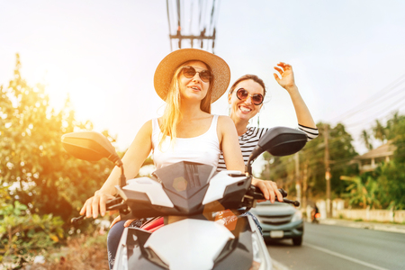 Happy smiling girlfreinds riding by motorbike in asian trafficの写真素材