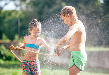 Two childs playing in garden, pours each other from the hose, makes a rain. Happy childhood concept image.の写真素材