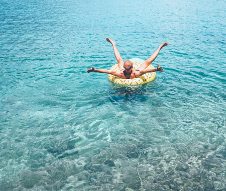 Man relaxing when swims on inflatable pineapple pool ring in crystal clear sea water. Careless vacation concept image.の写真素材