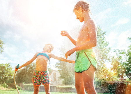 Brother and sister have fun, when play with watering hose in summer gardenの写真素材