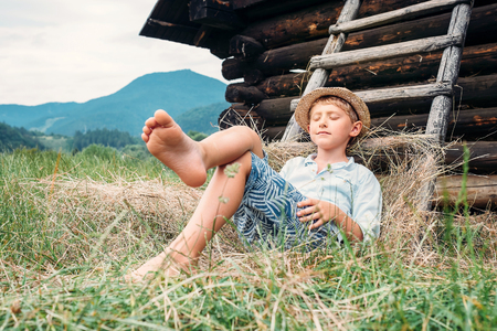 Boy in straw hat lies in hay near the barnの写真素材