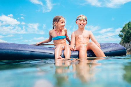 Sister and brother sitting on  inflatable mattress have fun when swim in the sea. Careless childhood time image.の写真素材