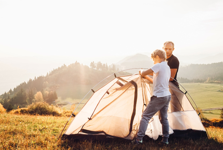 Father and son installing tent on forest glade.Trekking with kids concept imageの写真素材