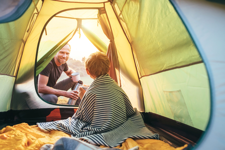Family lisure concept image. Father and son prepare for camping in mountain, drink tea in tentの写真素材