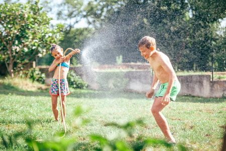 Two childs playing in garden, pours each other from the hose, makes a rain. Happy childhood concept image.の写真素材