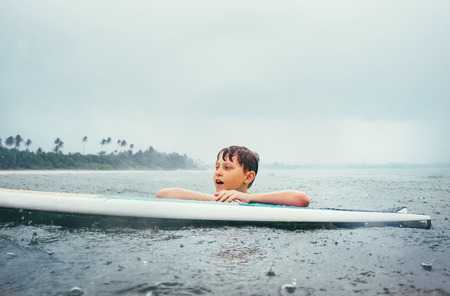 Boy learning to surf under the tropical rain. Surf school education concept image.の写真素材