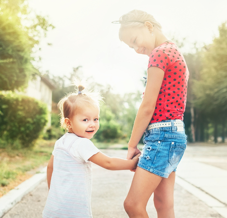 Two little sisters walking together in summer city park. Family values concept photo.の写真素材