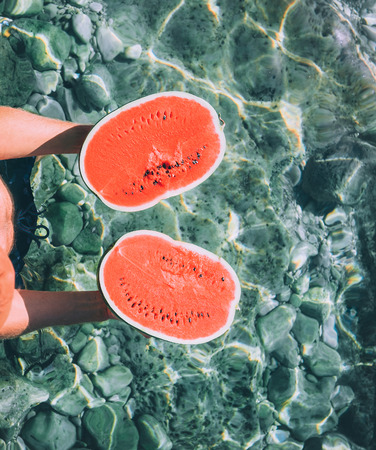 Man holds in hands two melon halfs and stands in crystal clear sea water. Healthy food concept imageの写真素材