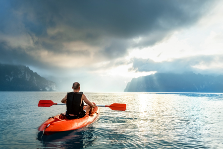 Man floating on kayak under sunrise sky on Cheow Lan Lake, Khao Sok national park, Thailandの写真素材