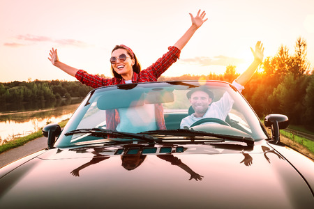 Traveling by car - happy couple in love go by cabriolet car in sunset timeの写真素材