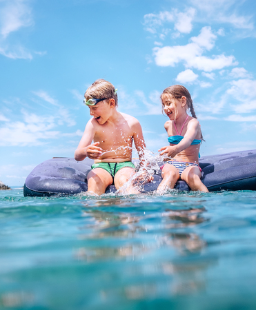 Sister and brother sitting on inflatable mattress and enjoying the sea water, cheerfully laughing when swim in the sea.の写真素材
