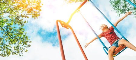 Funny smiling little girl swinging on the swing wide opened an arms with blue sky  headers web siteの写真素材