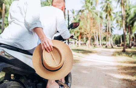 Happy woman riding motorbike with her boyfriend during their tropical vacation under palm trees Straw hat close up imageの写真素材