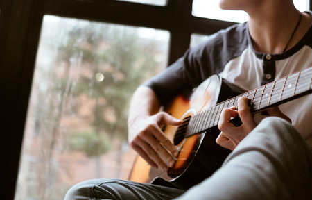 Man hands sitting on the big window windowsil and playing on guitar - fingers close up imageの写真素材