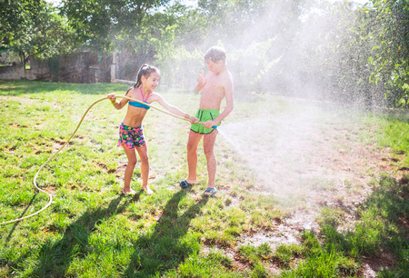 Brother and sister, playing with watering hose in hot summer afternoon on 
 family country house grass yard.の写真素材