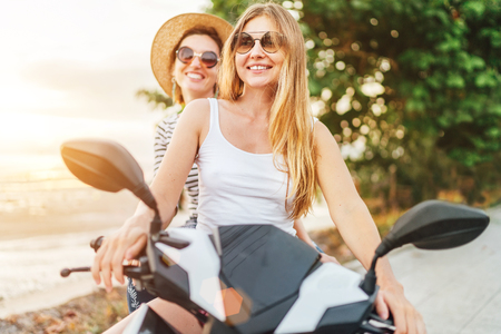 Two laughing girlfreinds motorbike travelers portrait behind the sunset sea coasの写真素材