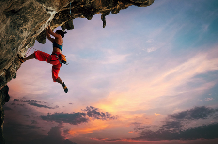 Athletic Woman climbing on overhanging cliff rock with sunset sky backgroundの写真素材