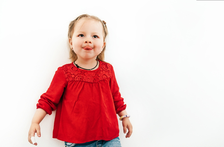 Happy emotional little girl in red blouse showing tongue. White background studio shoot.の写真素材