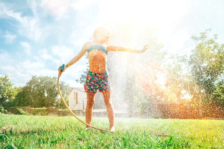 Cute little girl refresh herself from garden watering hoseの写真素材