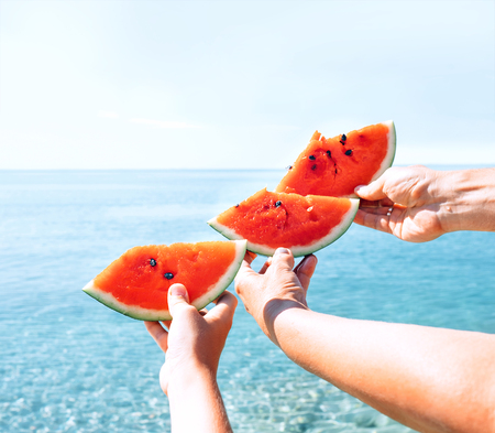 Three hands with watermelon segments are on azure calm sea water backgroundの写真素材