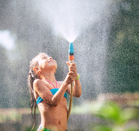 Cute little girl pours herself from the hose, makes a rain. Hot summer day pleasureの写真素材