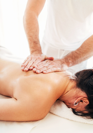 Masseur man doing massage manipulations on the scapula area zone during massaging female bodyの写真素材