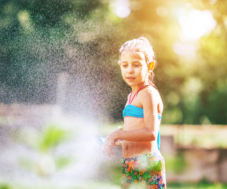 Little Cute girl sprinkls a water for herself from the hose, makes a rain. pleasure for hot summer days. Happy careless childhood concept image.の写真素材