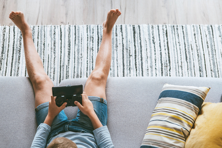 Boy sits on sofa plays with smartphone and gamepad camera top view. Child and electronic devices conceptの写真素材