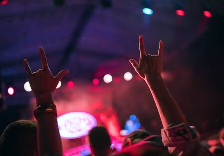 Young teenager girl raised up two hands with sign of the horns gesture supporting favorite rock band on the night concertの写真素材