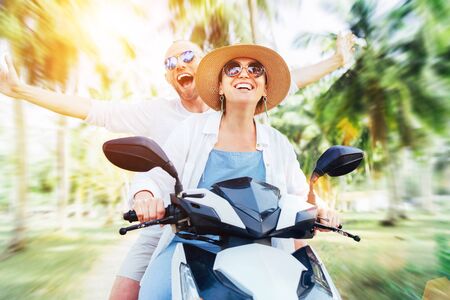 Happy cheerful smiling couple travelers riding motorbike scooter under palm trees. Tropical vacation  concept imageの写真素材