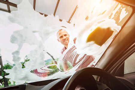 Man washes car front windows with soap foamの写真素材