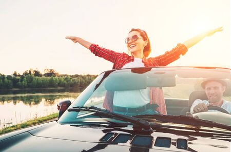 Happy couple in love go by cabriolet car in sunset timeの写真素材