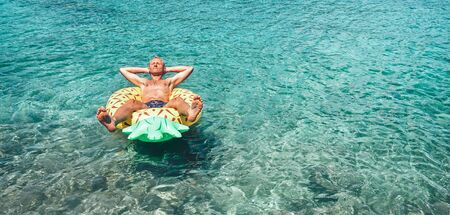 Man relaxing when swims on inflatable pineapple pool ring in crystal clear sea water. Careless vacation concept image.の写真素材