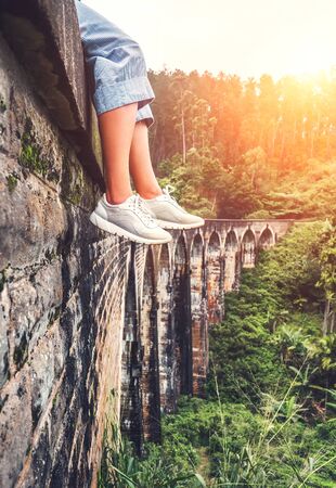 Female tourist sits on the Demodara nine arches bridge in Ella, Sri Lanka: close up feet imageの写真素材