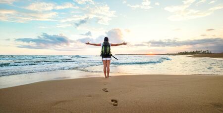 Woman backpacker greeting a sunset at the ocean coastの写真素材