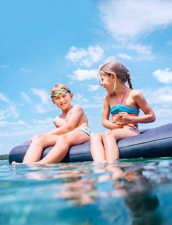 Sister and brother sitting on  inflatable mattress and enjoying the sea waterの写真素材