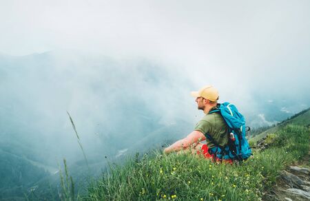 Backpacker man has a rest break enjoying cloudy valley bottom walking by the foggy cloudy weather...