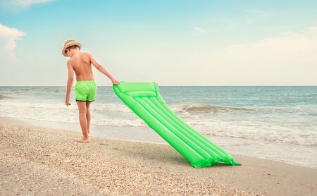 Boy with swimming mattress walks on sand sea beachの写真素材