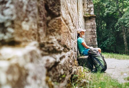Tired female backpacker resting on the bench near the old antique brick wall castle on the famous Camino de Santiago way.の写真素材