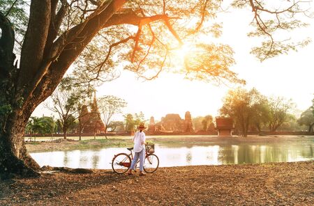 Female traveler weared light summer clothes and hat have early morning walk with bicycle near pond in Ayutthaya historical park,Thailandの写真素材