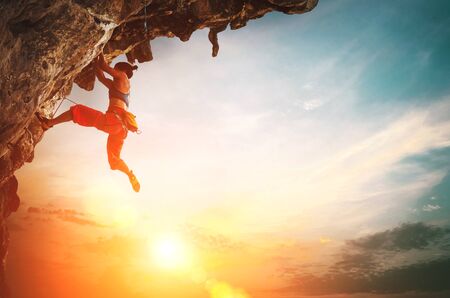 Athletic Woman climbing on overhanging cliff rock with sunset sky backgroundの写真素材