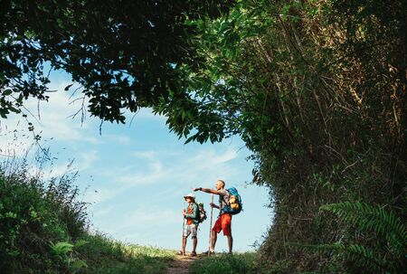 Father and son backpackers hiking by the forest pathway, taking a short rest break. Happy parents travelling with kids concept image.の写真素材