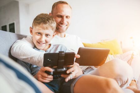 Father and son portrait with electronic devices playing. Sitting at home in cozy atmosphereの写真素材