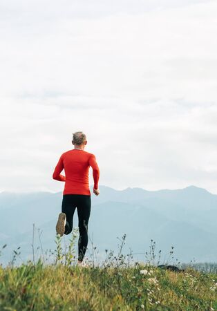 Man dressed in red long sleeve shirt runs by the road with mountain background vertical shoot.の写真素材