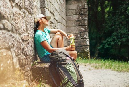 Very tired female backpacker resting on the bench near the old antique brick wall castle on the famous Camino de Santiago way.の写真素材